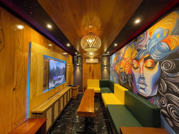 A cozy lounge area with wooden walls, a large TV screen, a wooden bench, and colorful artwork on the walls. - Diwata Nature Resort (San Pablo)