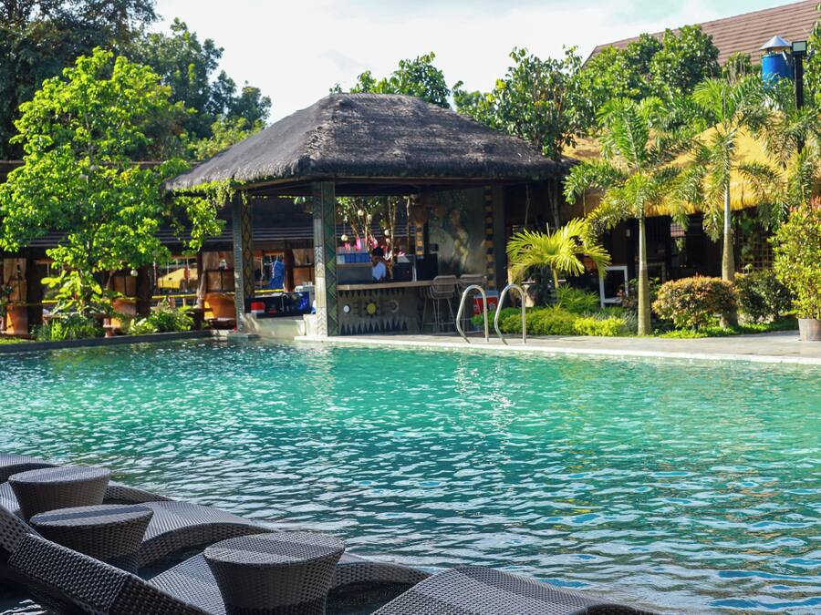 A pool with lounge chairs, a bar area, and a thatched-roof structure.