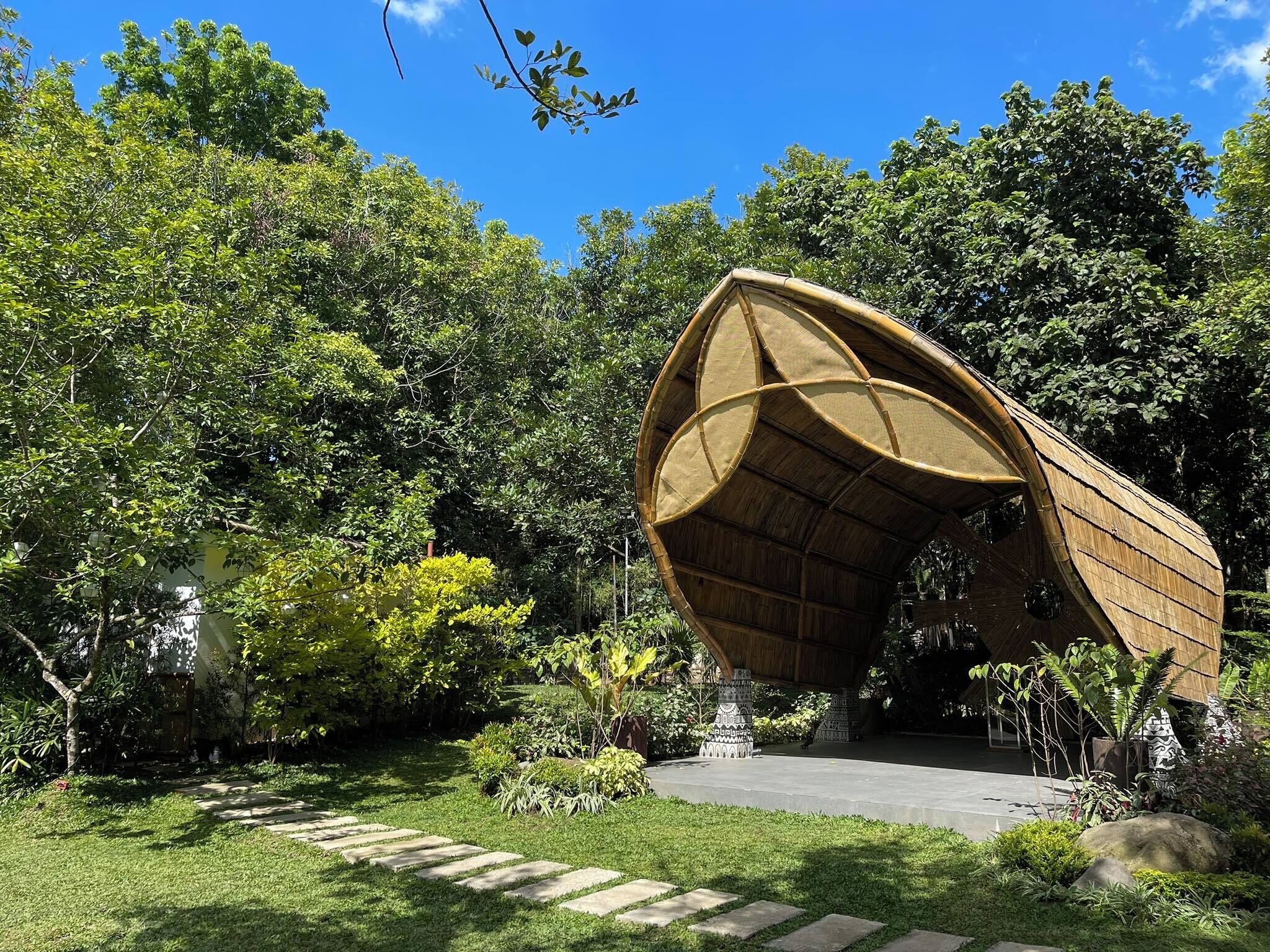 A unique architectural structure with a curved roof, surrounded by lush greenery and a clear blue sky.