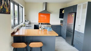 A modern kitchen with a central island, grey cabinets, and a red backsplash. - Sunny, family-friendly house with harbour views (Wellington)