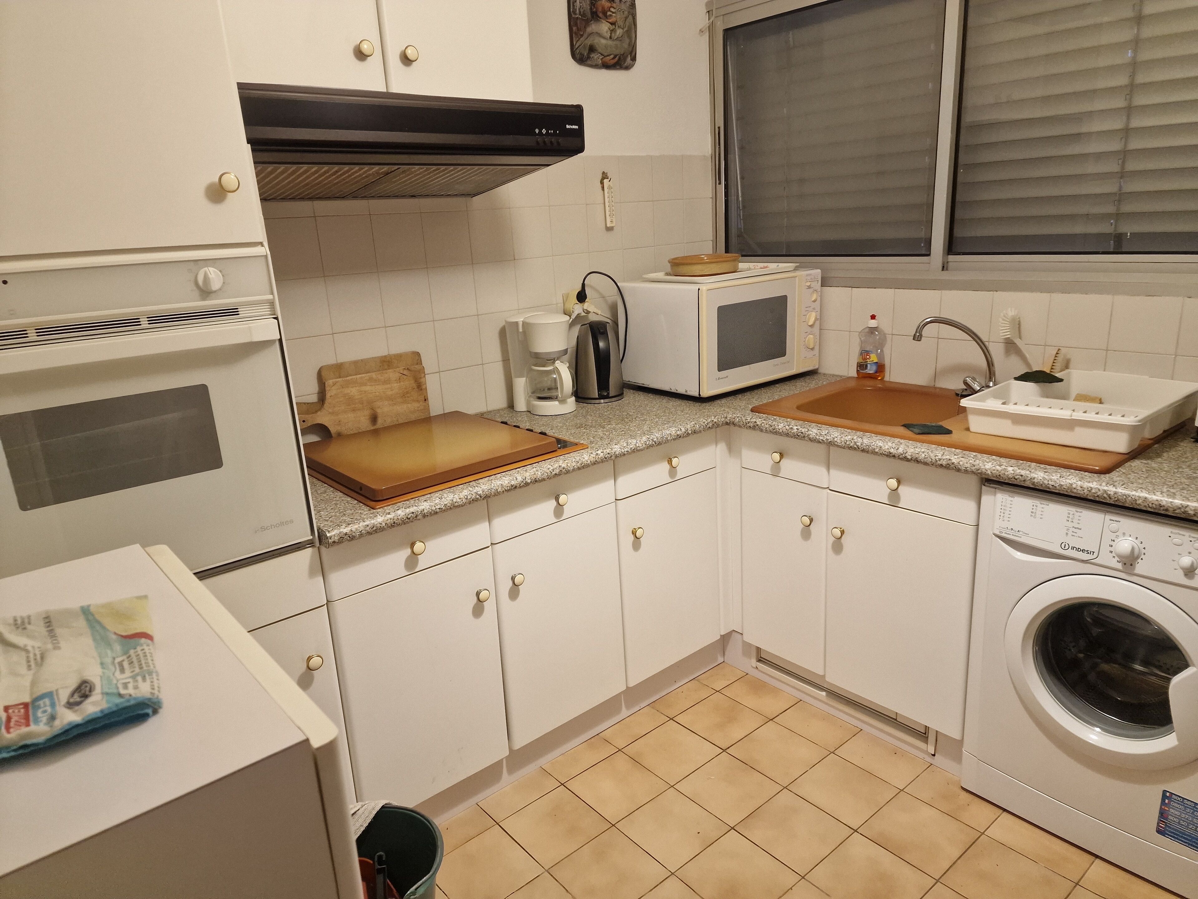 A compact kitchen with white cabinets, a built-in oven, a microwave, a coffee maker, and a washing machine.