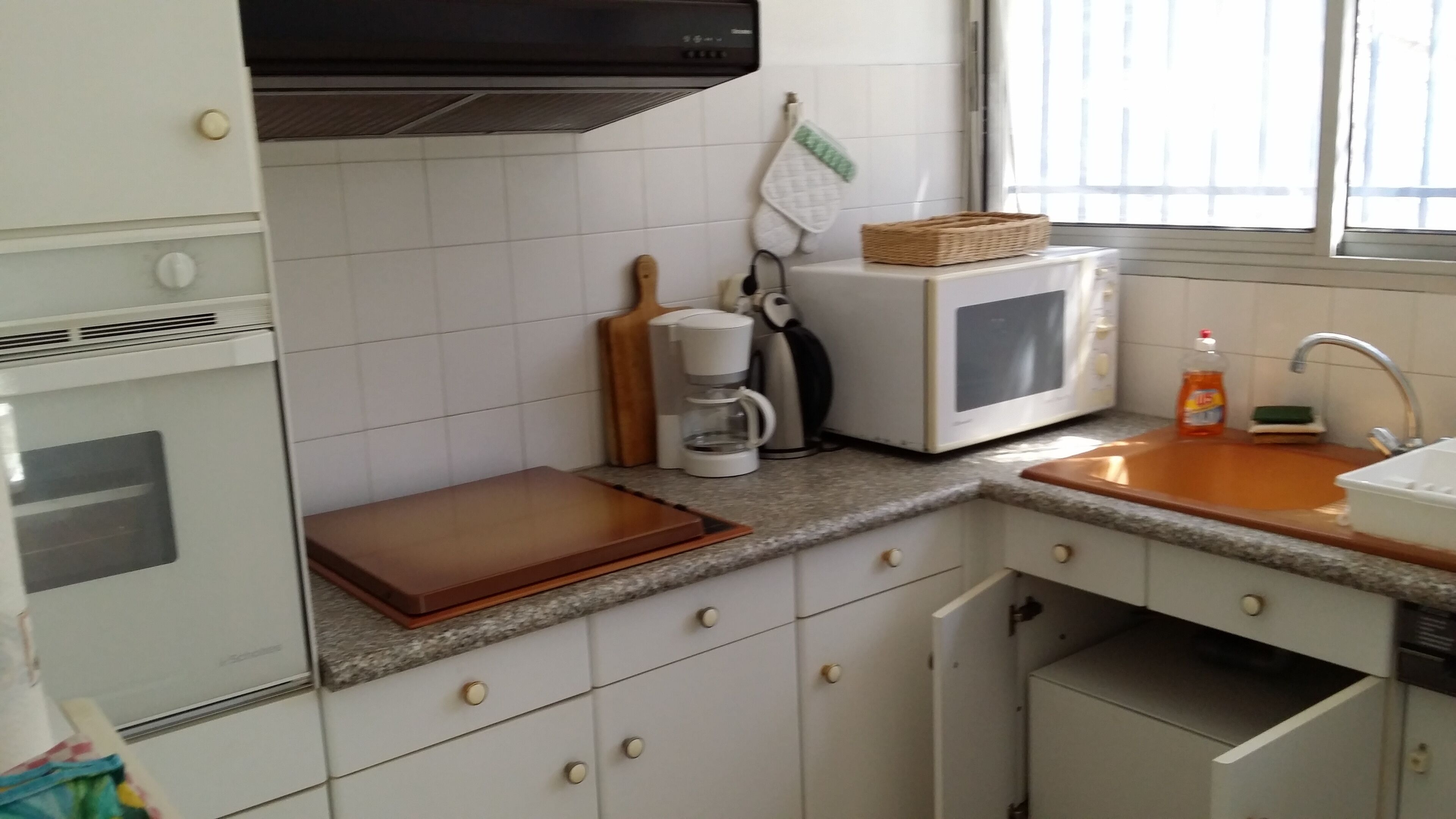 A kitchen with white cabinets, a microwave, a coffee maker, and a sink.
