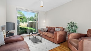 Un salon moderne avec un canapé en cuir marron, une table basse en verre et une grande porte-fenêtre coulissante donnant sur un jardin.