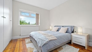 Une chambre à coucher avec un lit, des tables de chevet, une fenêtre et un radiateur.