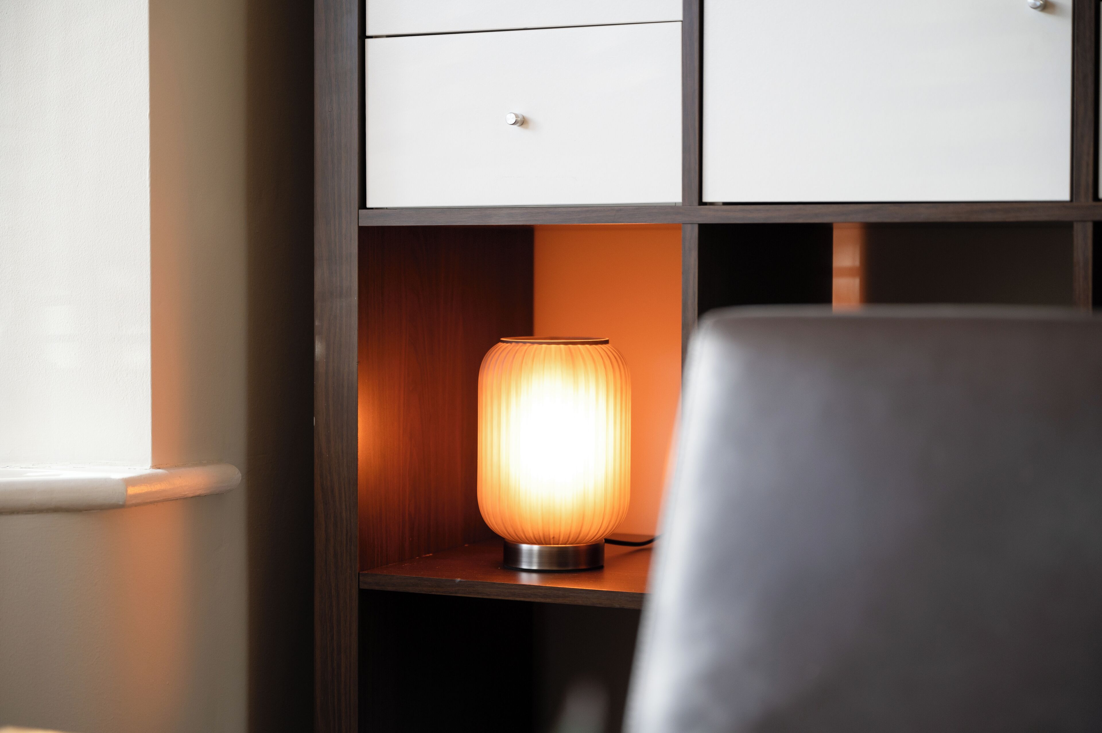 A room with a wooden cabinet, a white drawer, and a lit table lamp.