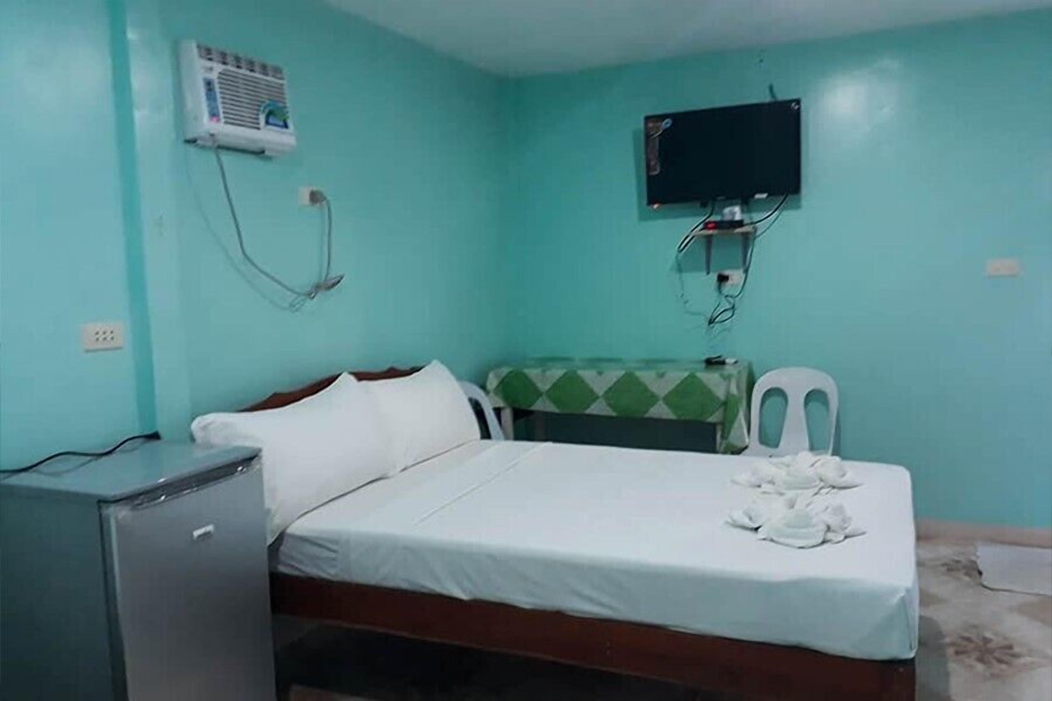 A small, single-bed room with a bed, a desk, a chair, a television, and a refrigerator.