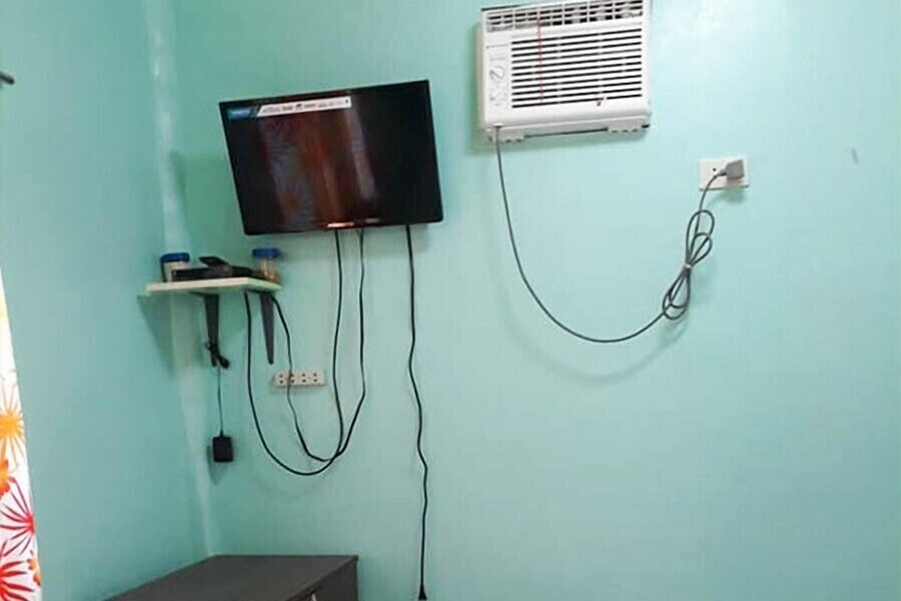A room with a flat-screen TV mounted on the wall, an air conditioning unit, and a power outlet.
