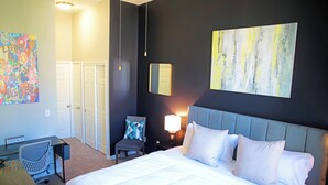 A hotel room with a bed, desk, chair, and artwork on the walls.