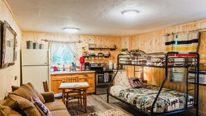 Una habitación pequeña con literas, kitchenette, comedor y sofá.