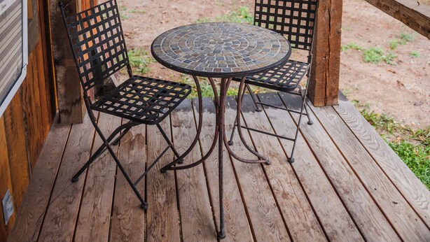 Una terraza de madera con una mesa y dos sillas, con vista a un área verde con árboles.
