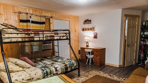 Una cama litera con un edredón estampado, un escritorio con una silla, una lámpara y una pequeña alfombra.
