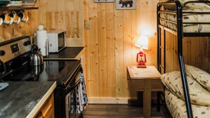 Una habitación compacta con paneles de madera, una cama litera, un kitchenette y una pequeña mesa con lámpara.