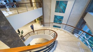 Un interior de varios niveles con una escalera curva, suelo de mármol y obras de arte en las paredes.