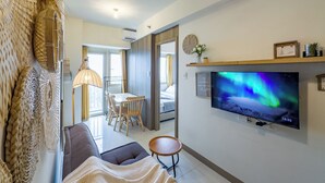 A modern living room with a flat-screen TV, a sofa, a dining area, and a view of the outdoors. - GemstoneBR in SMDC Coast Residences (Pasay)