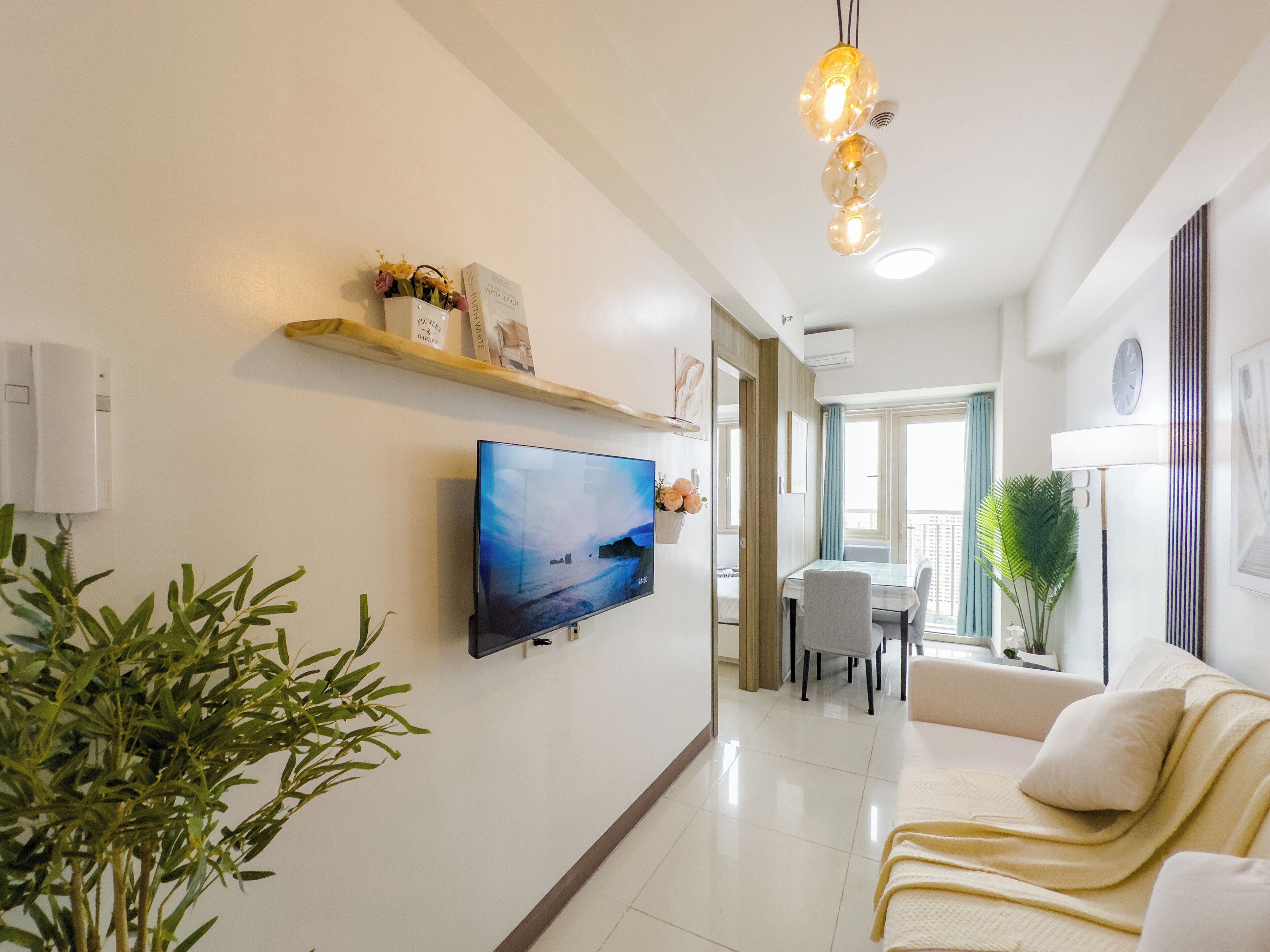 A modern living room with a flat-screen TV, a sofa, a dining table, and a potted plant.