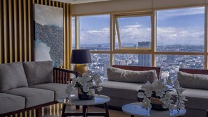 A modern living room with a sofa, two side tables with orchids, a lamp, and a large window with a city view. - GemstoneBR in SMDC Coast Residences (Pasay)