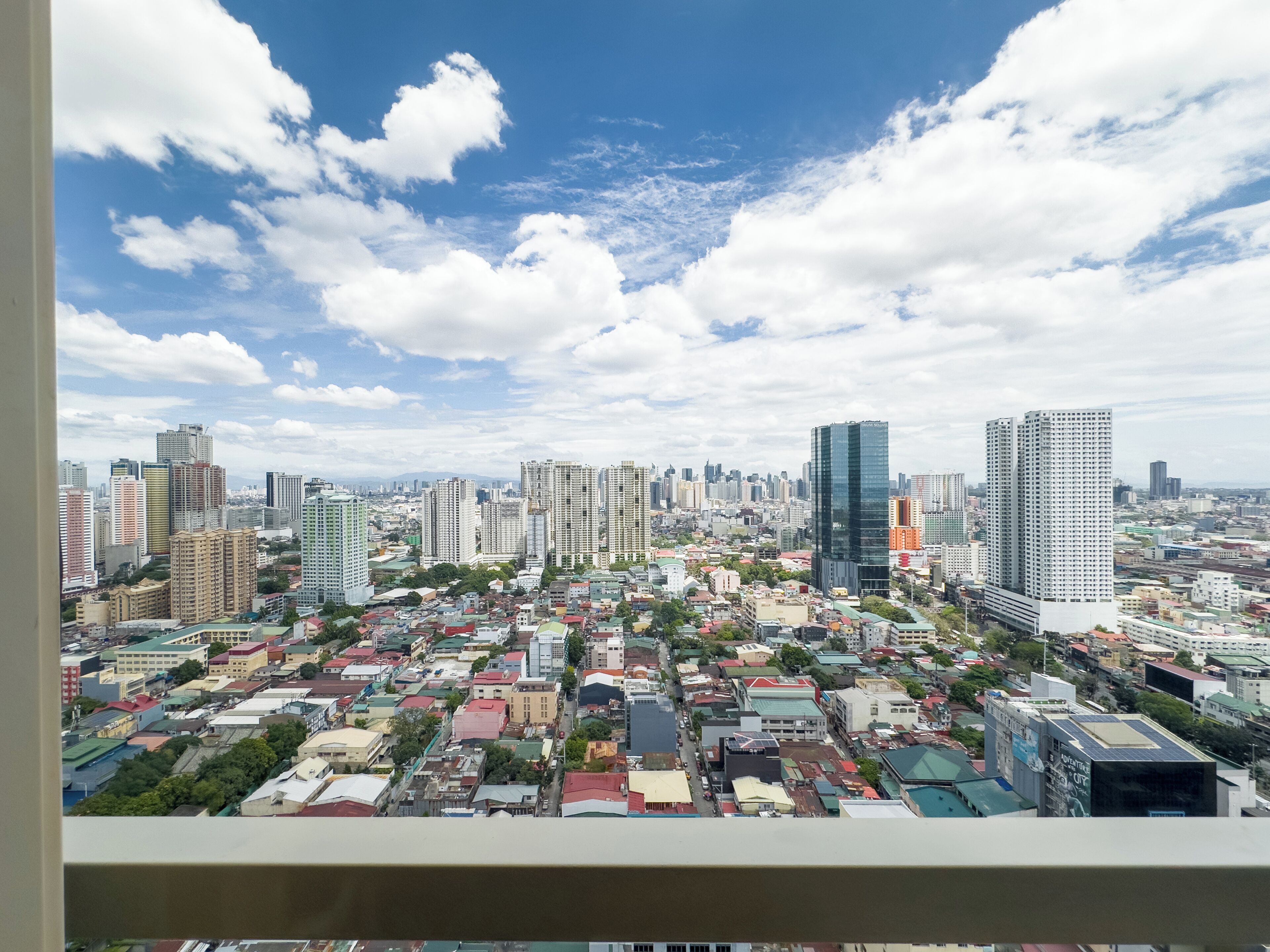 A cityscape with a mix of high-rise and low-rise buildings, a variety of roof colors, and a clear sky with scattered clouds.