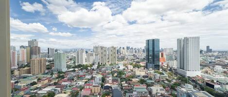 A cityscape with a mix of high-rise and low-rise buildings, a variety of roof colors, and a clear sky with scattered clouds.