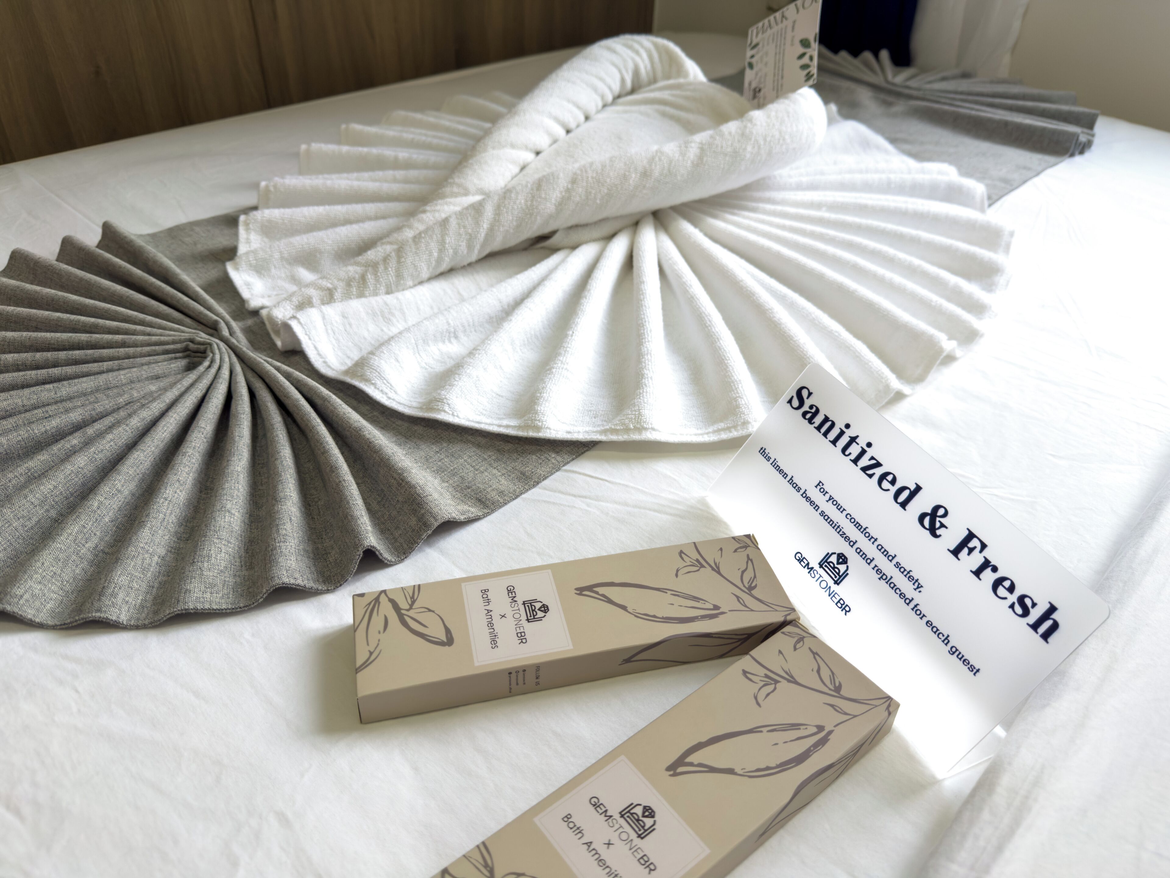 A bed with neatly folded linens, a 'Sanitized & Fresh' label, and a 'GemstoneBR' box.