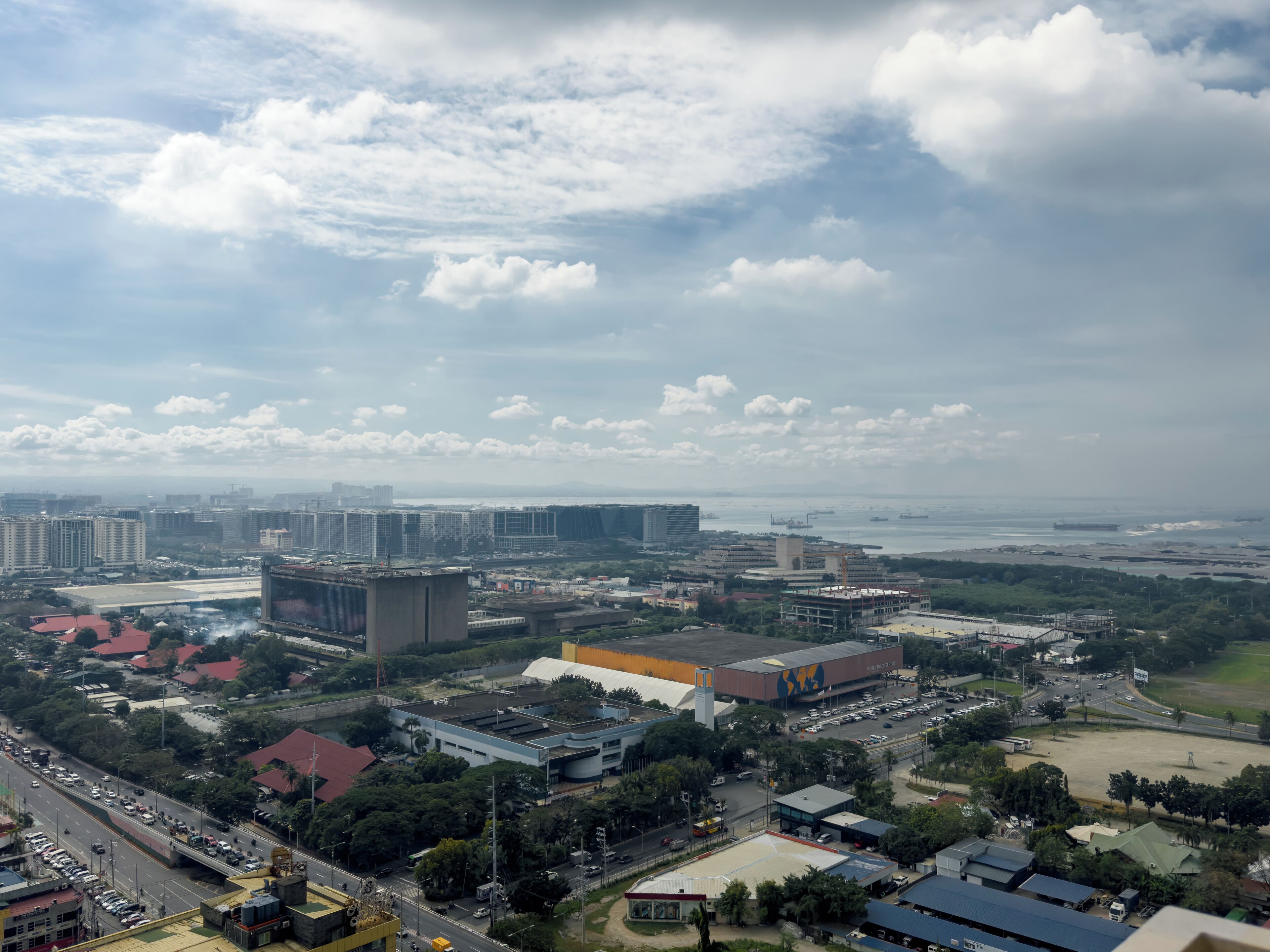 A cityscape with high-rise buildings, a large commercial building, and a view of the sea.