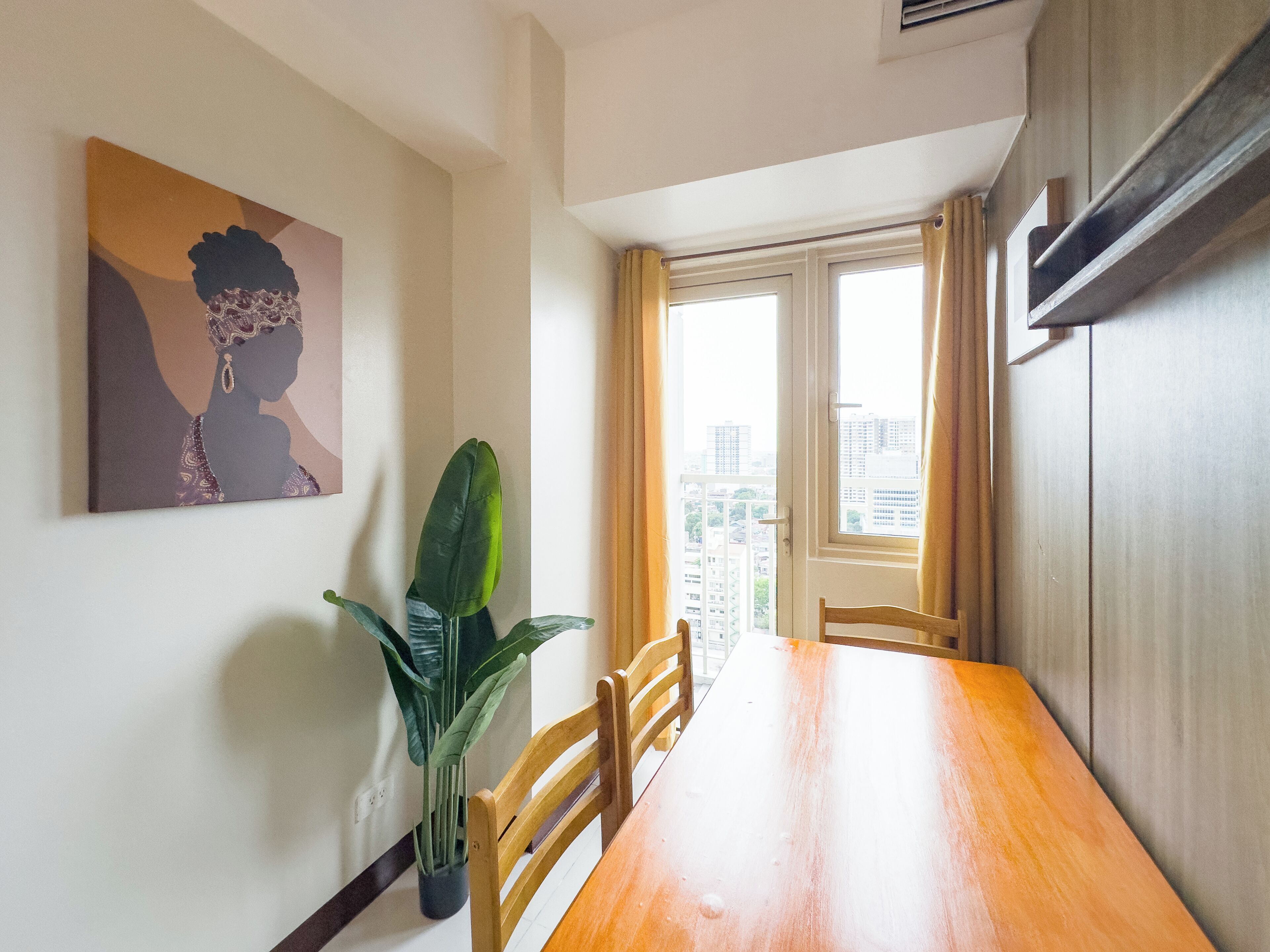 A dining area with a wooden table, chairs, a potted plant, and a painting on the wall.
