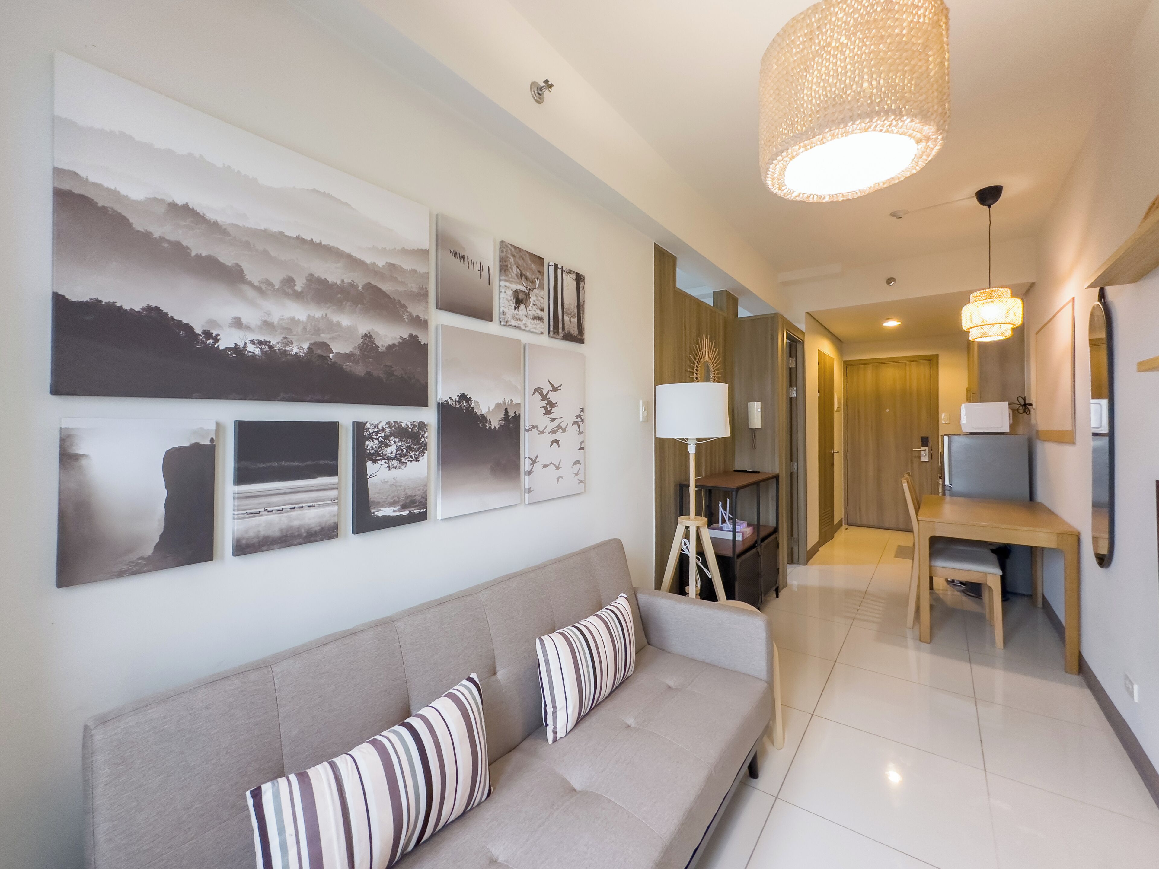 A modern living room with a sofa, a dining area with a table and chairs, and a hallway leading to a door.