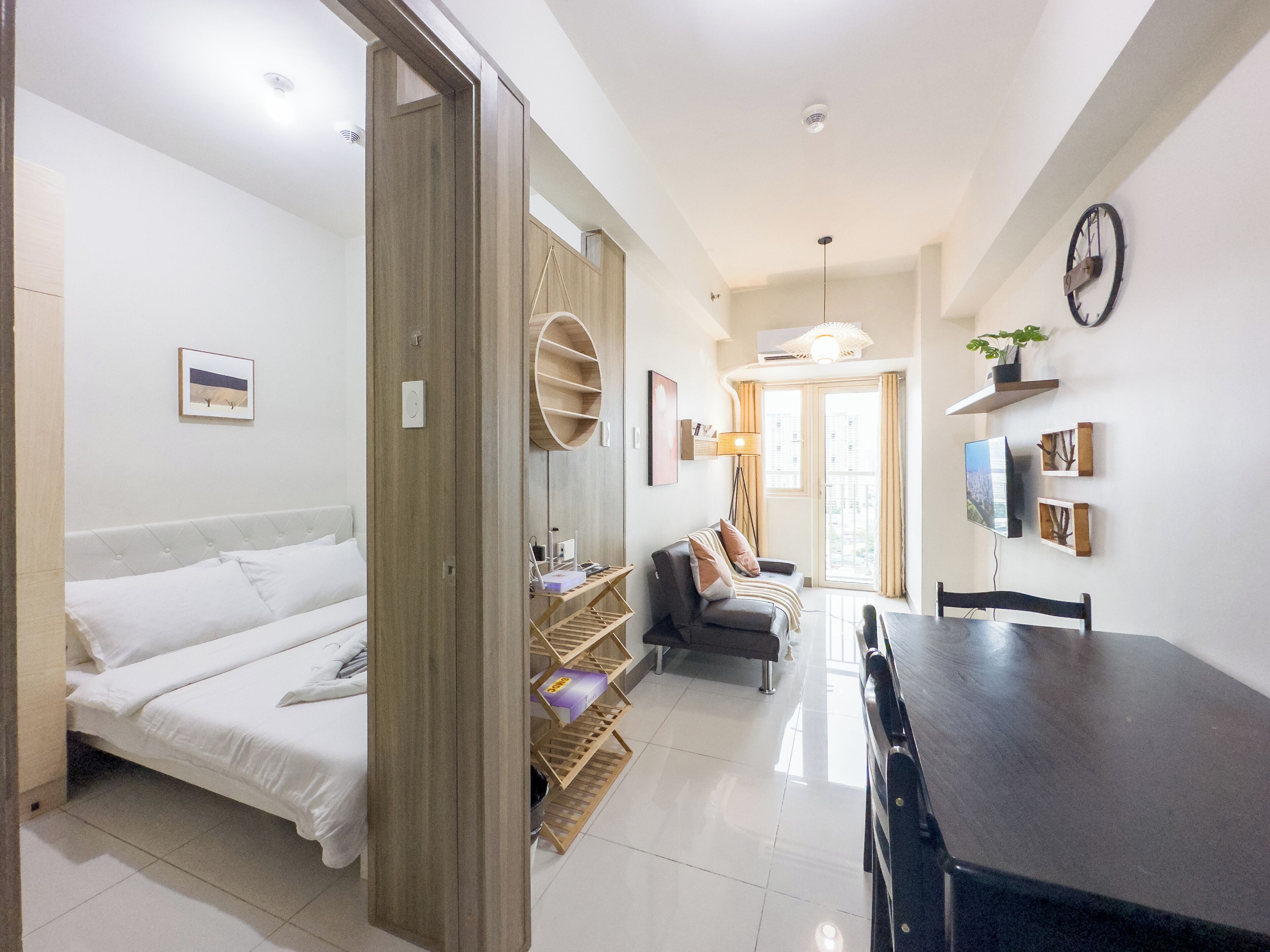 A modern, well-lit room with a bed, a sofa, a dining table, and a TV.