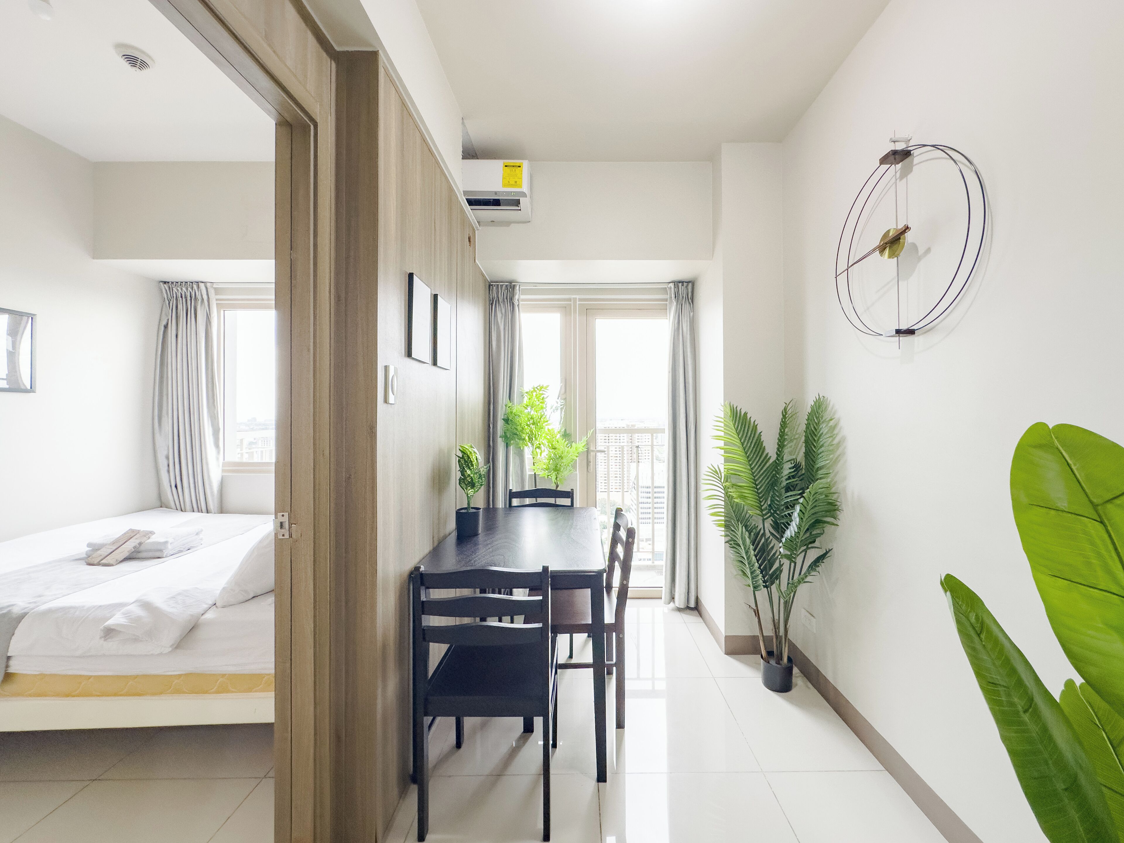 Une chambre d’hôtel moderne, équipée d’un lit, d’une table à manger avec des chaises, d’une plante en pot et d’un climatiseur fixé au mur.
