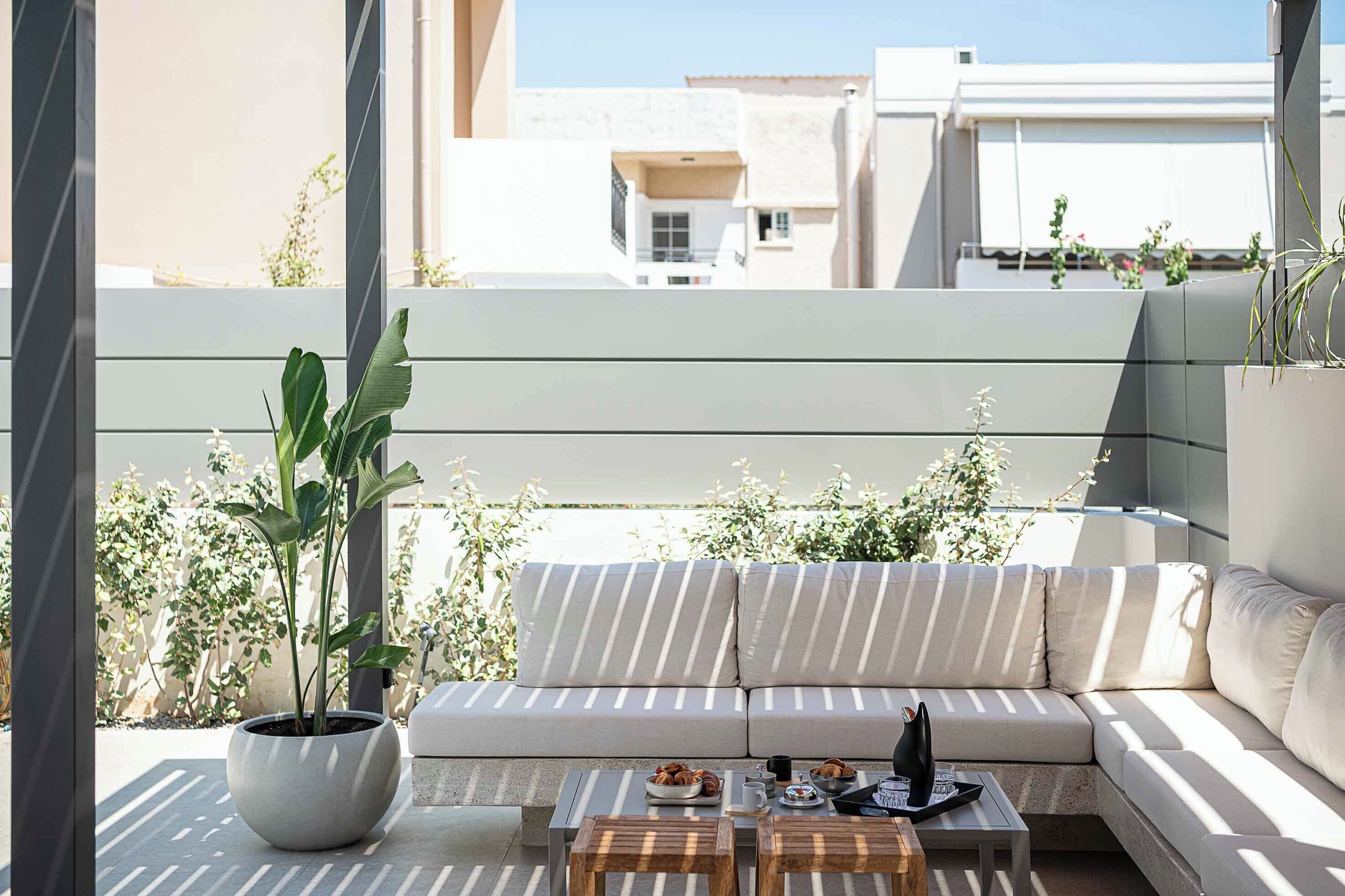 Un balcón con un sofá a rayas, una planta en maceta y una mesita con una bandeja de aperitivos.