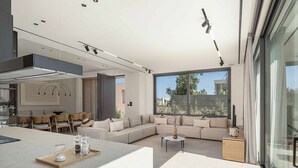 A modern living room with a sofa, coffee table, and dining area. - Sancy Luxury Villa 400m beach, Heated* pool & Gym (Chania)