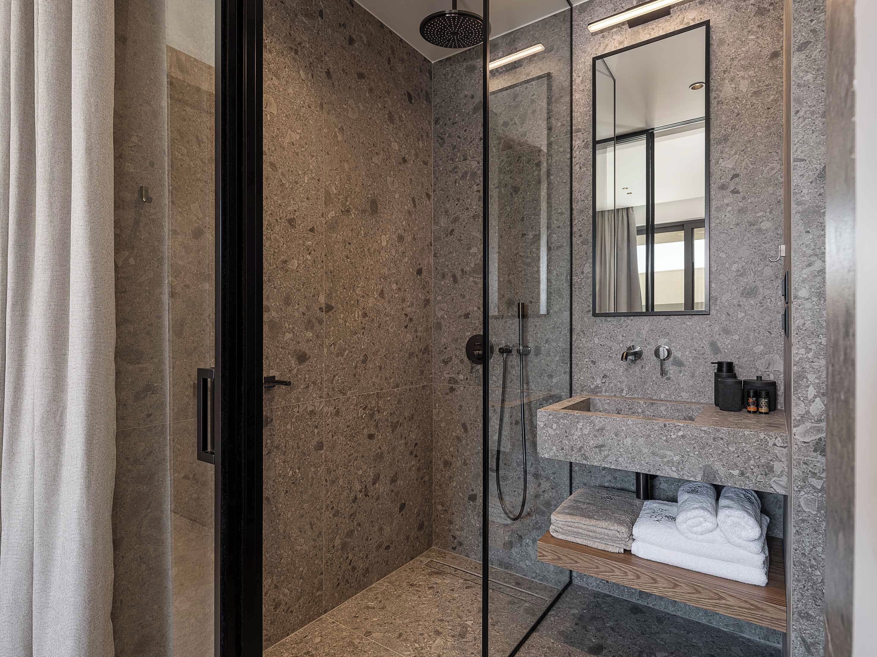 Un baño moderno con cabina de ducha de vidrio, lavamanos de mármol y un espejo arriba.