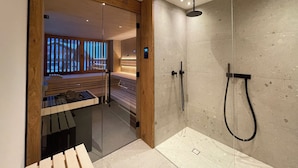 Une salle de bain moderne dotée d’une douche à parois de verre, d’un banc en bois et d’un espace sauna visible.