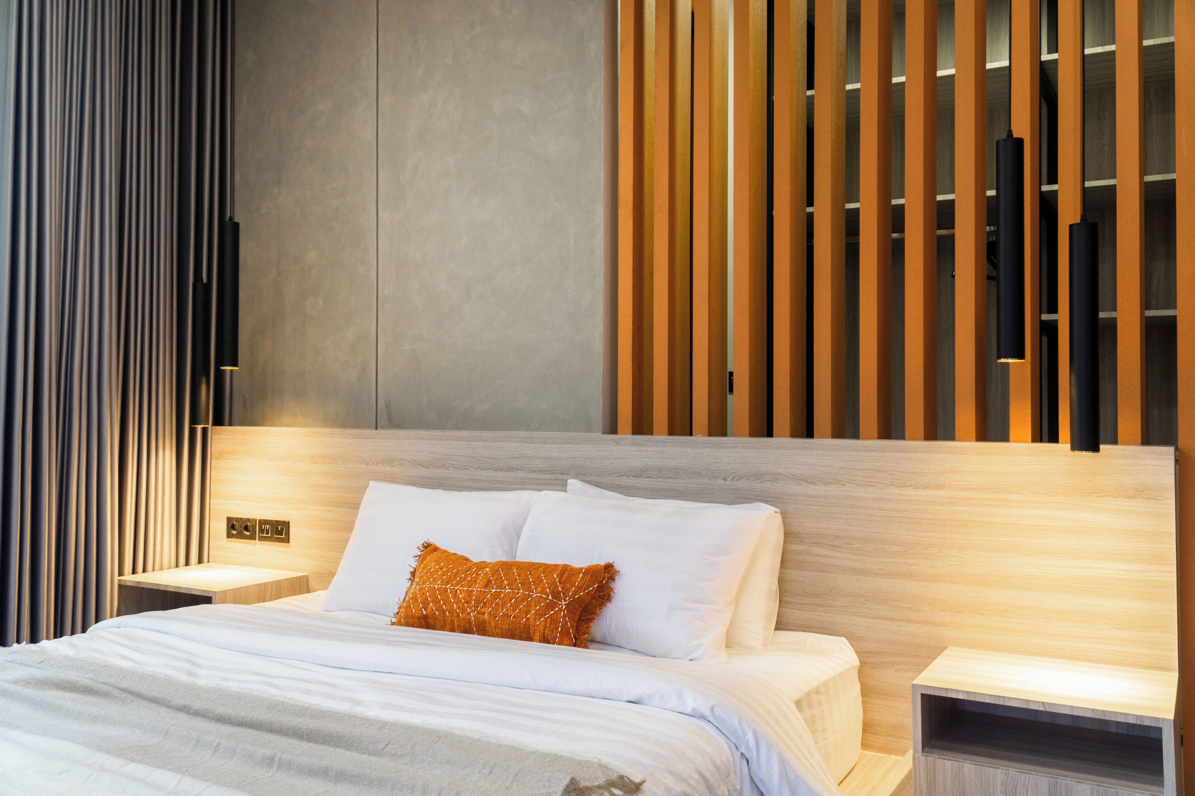 A modern hotel room with a wooden headboard, white bedding, and a nightstand with a lamp.