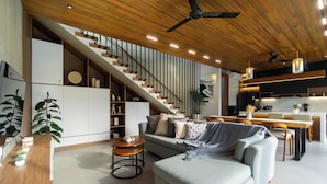 Un salon moderne avec un canapé gris, une table basse en bois et un escalier menant à un espace cuisine.