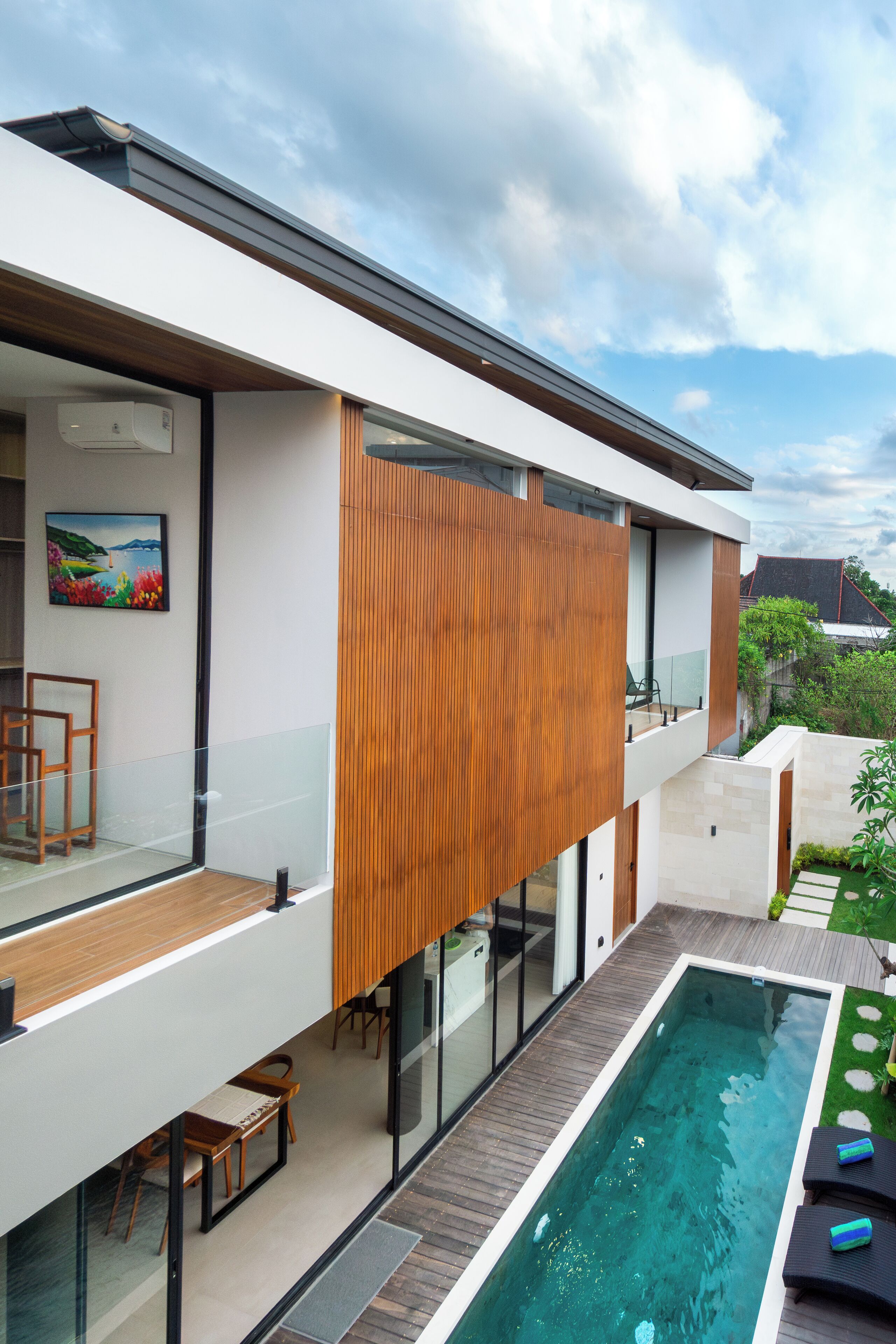 A modern house with a glass balcony, a swimming pool, and a wooden deck.