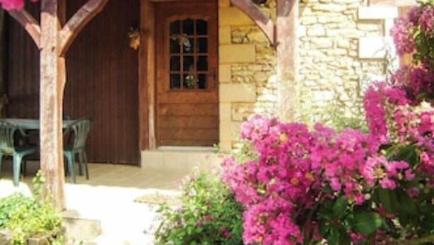 Een stenen gebouw met een houten deur en een raam, omgeven door felroze bougainvillea bloemen.