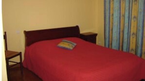 Een slaapkamer met een rood sprei, een houten hoofdbord, twee nachtkastjes en een raam met blauwe gordijnen.