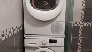 Pesu- ja kuivauskoneet on asennettu päällekkäin kylpyhuoneeseen, jossa on laatoitetut seinät ja erillinen suihkutila.