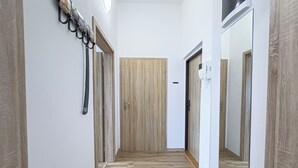 Käytävä, jossa on puulattia, valkoiset seinät ja puinen ovi käytävän päässä.