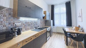 Moderni keittiö, jossa on laatoitettu välitila, puukaapit, sisäänrakennettu uuni sekä ruokailutila, jossa on pöytä ja tuolit.