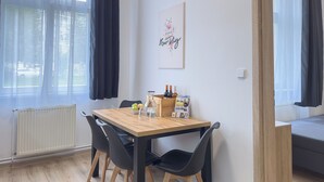 Ruokailutila, jossa on puinen pöytä, mustat tuolit, hedelmäkulho, pulloja ja lasinen kannu.