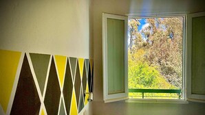 A room with a geometric-patterned wall, a window with an open view of trees, and a wooden bench. - Hotel Splendor (Tortoli)