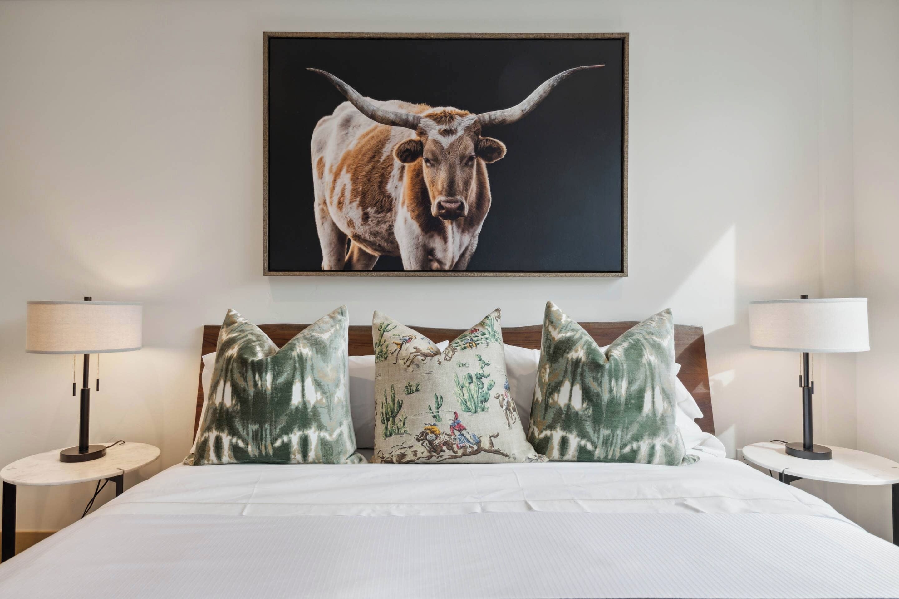 Une chambre d’hôtel avec un grand lit, deux lampes de chevet et un tableau représentant un taureau au mur.