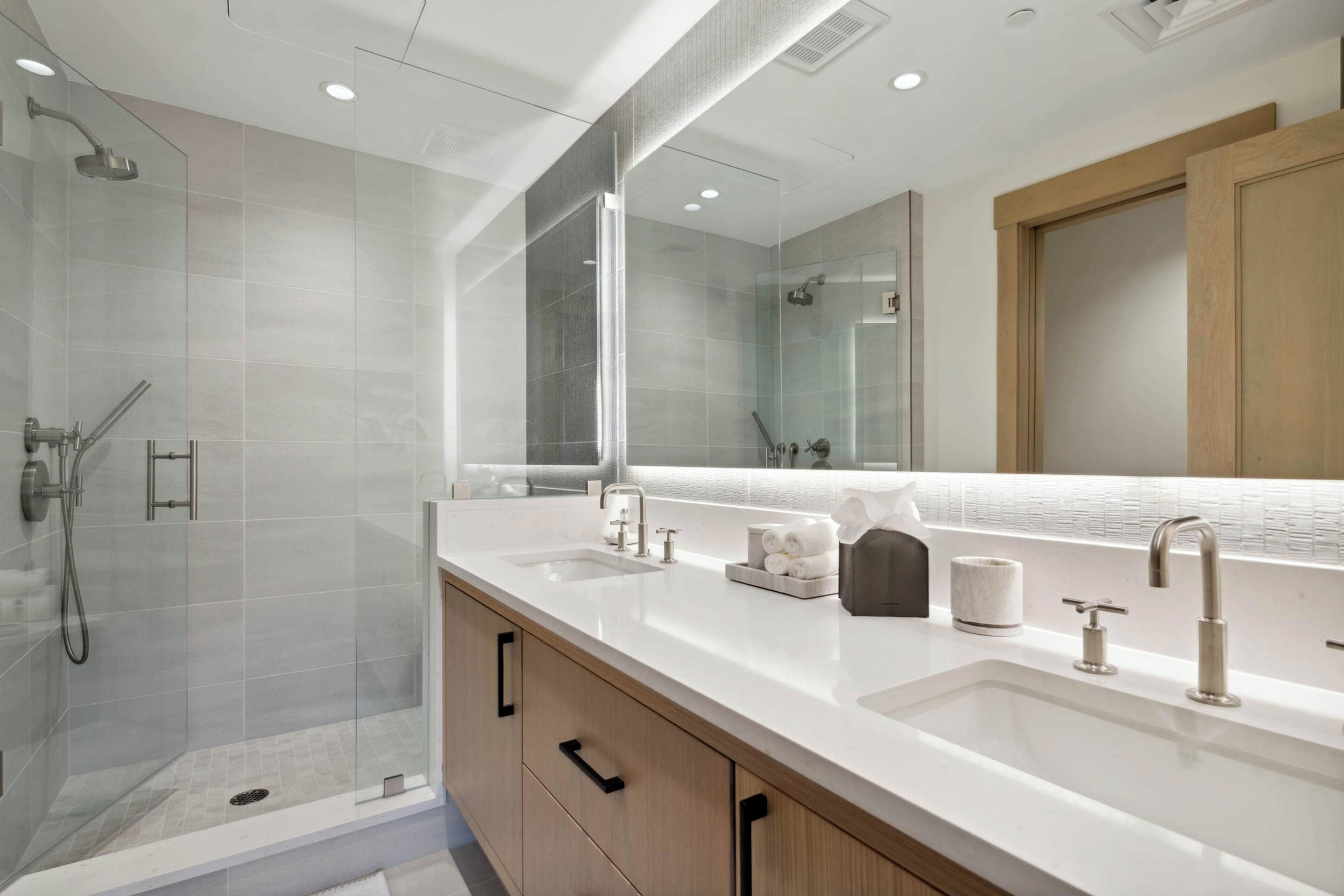 A modern bathroom with a glass-enclosed shower, a large mirror, and a white vanity with a sink and towel rack.