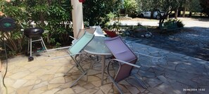 Un patio con una mesa redonda y sillas, una parrilla y un suelo de baldosas de piedra.