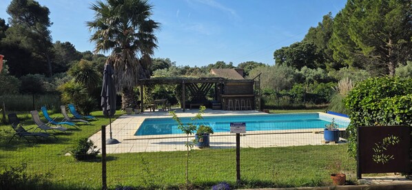 Una piscina con sillas de descanso, una pérgola y una zona vallada.