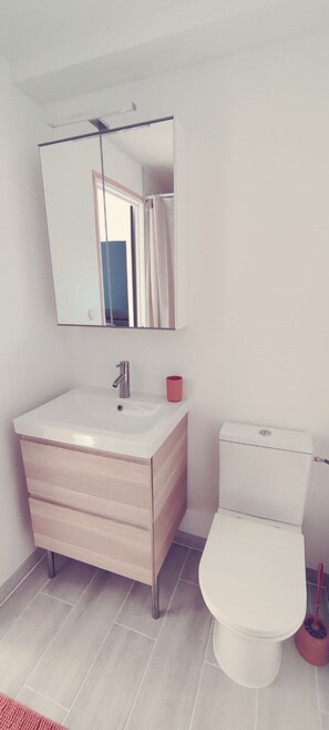 Un baño moderno con lavamanos, espejo y inodoro blancos.