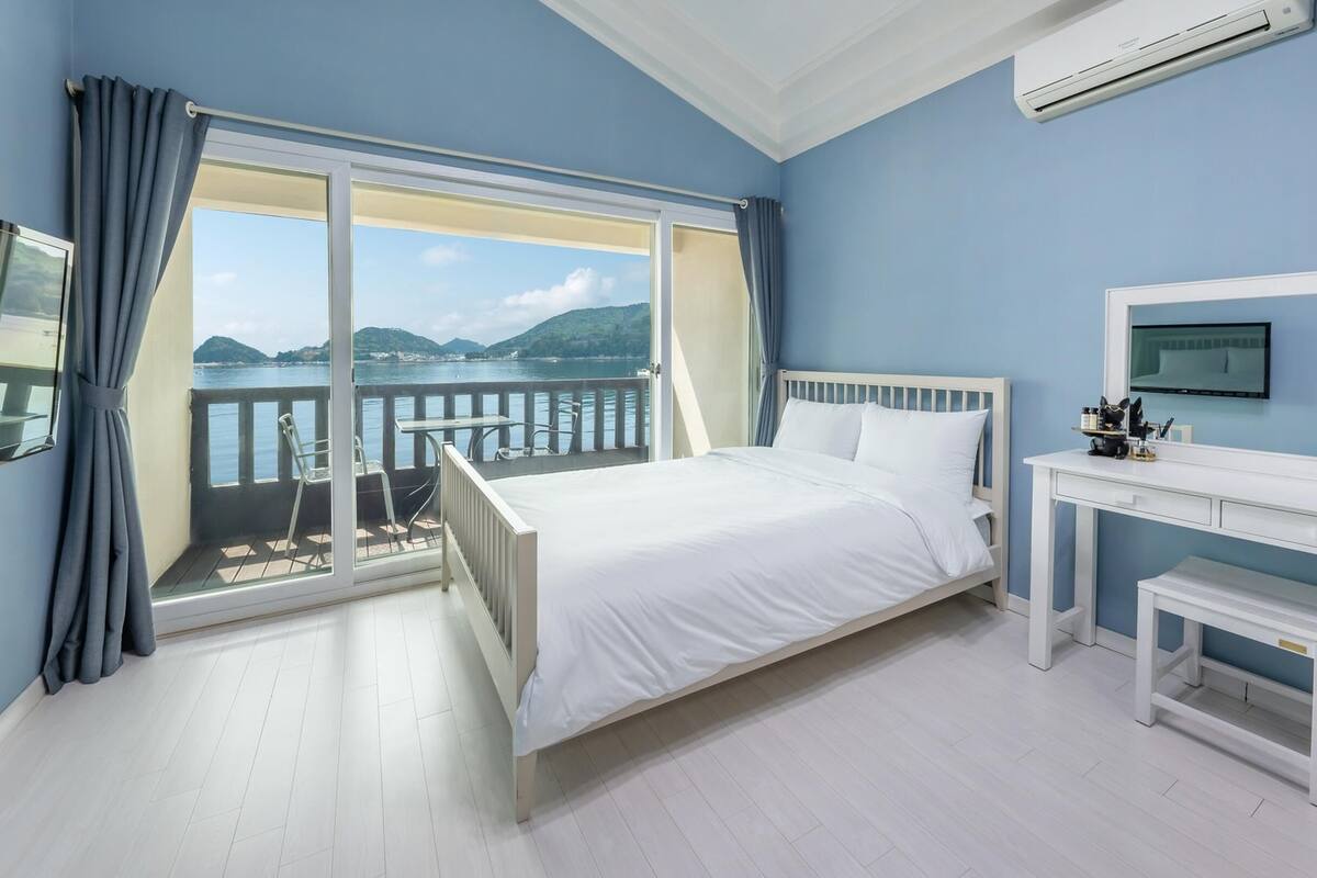 Un dormitorio con cama, escritorio, silla y vista al mar.
