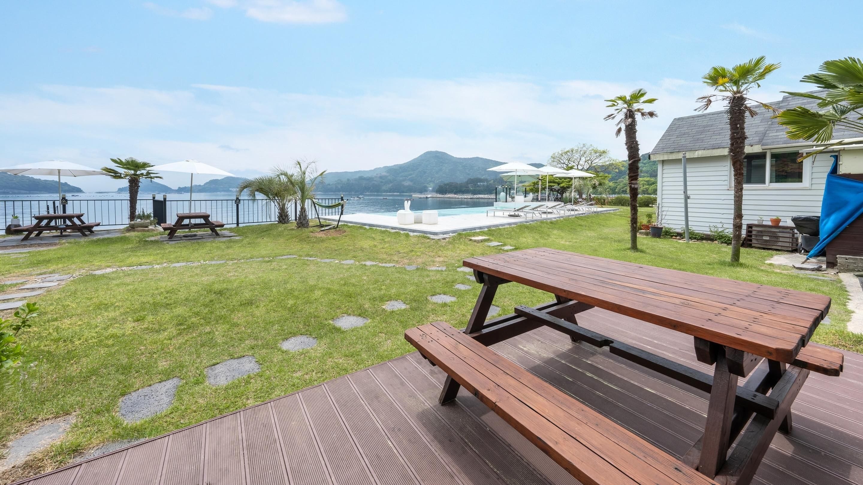 Patio con terraza de madera, mesas de picnic, piscina y vistas al mar y las montañas.