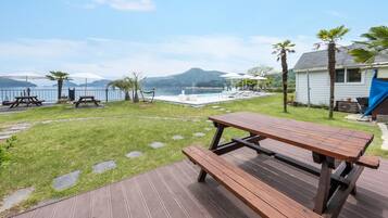 Patio con terraza de madera, mesas de picnic, piscina y vistas al mar y las montañas.